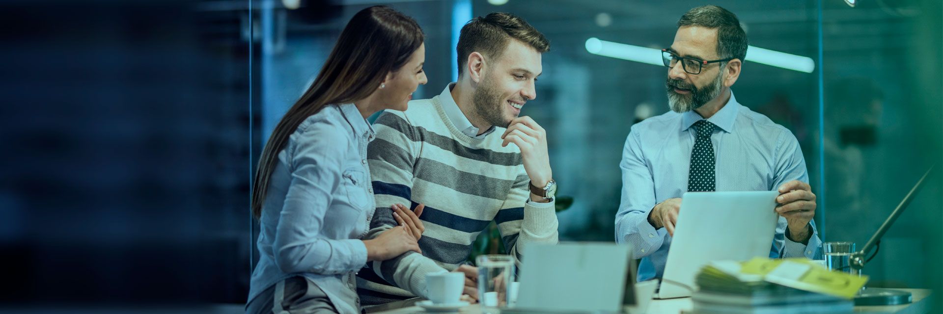 Three professionals engaged in a discussion around a laptop in a modern office setting.