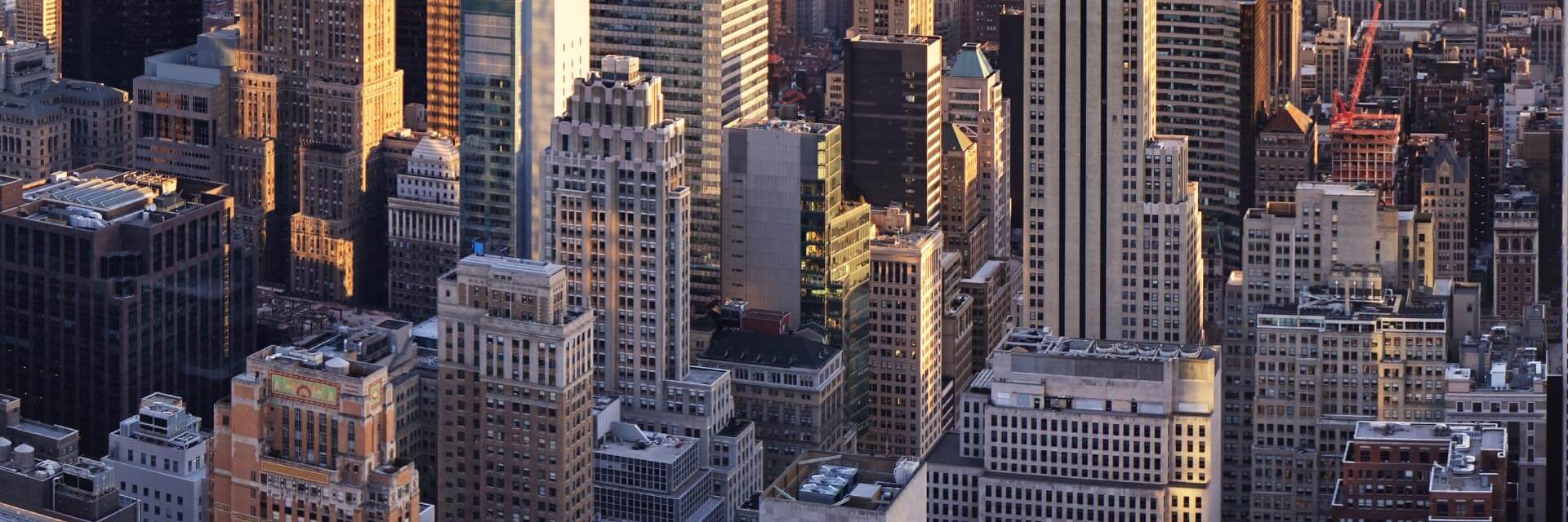 City skyline featuring various skyscrapers with sunlight reflecting off glass surfaces and rooftops.