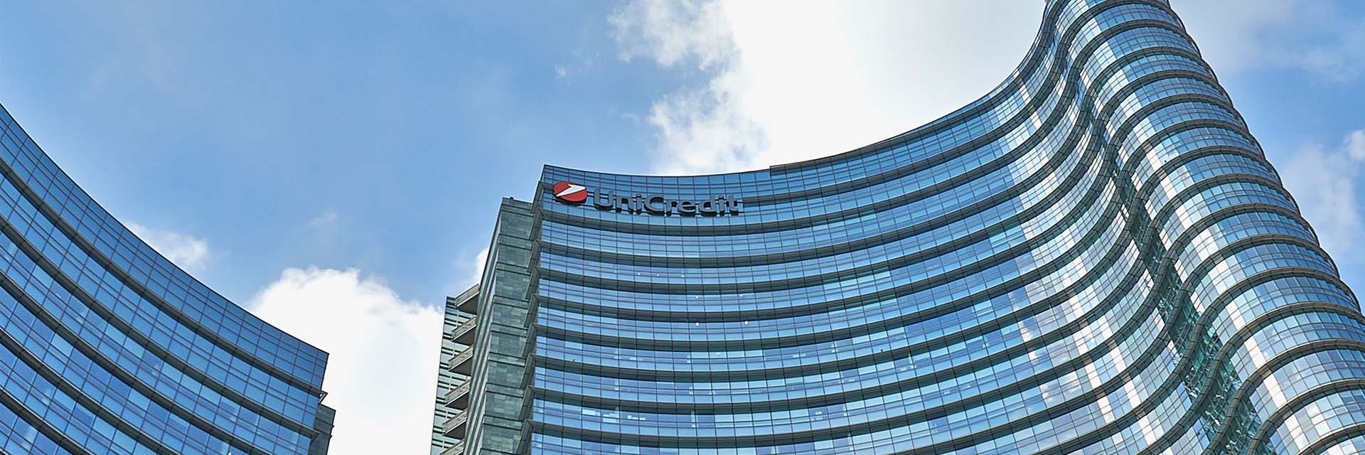 Glass skyscraper with curved facade and “UniCredit” sign against a blue sky.