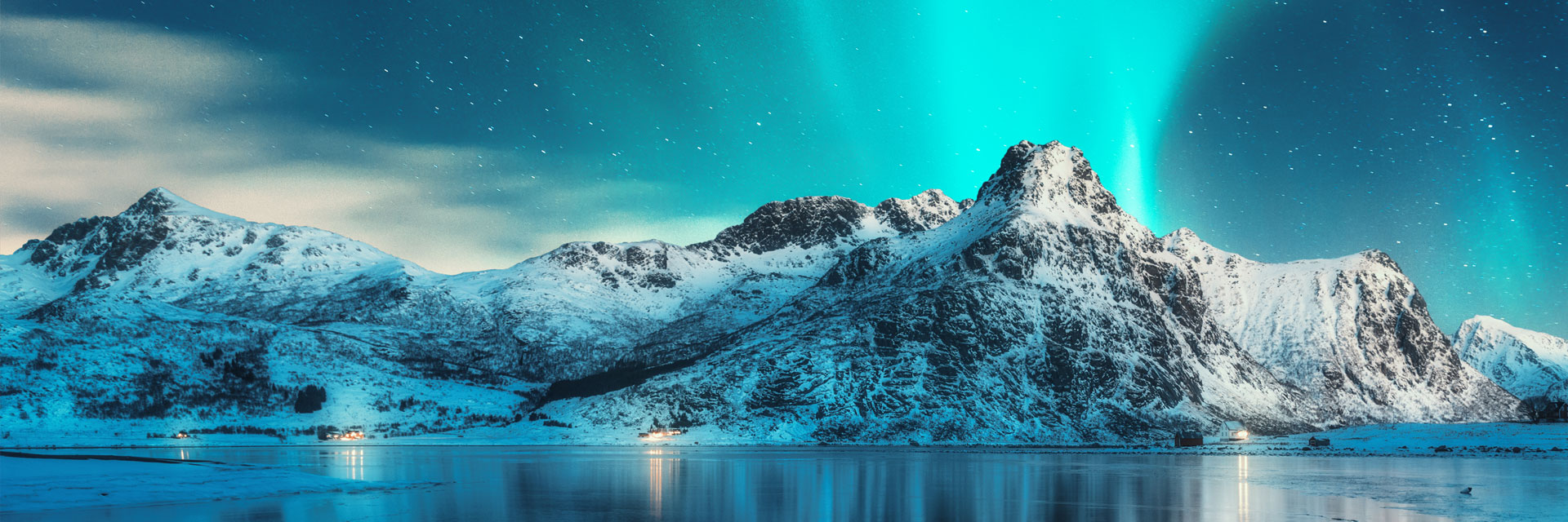 Snow-covered mountains under a night sky illuminated by the northern lights, with a calm lake reflec